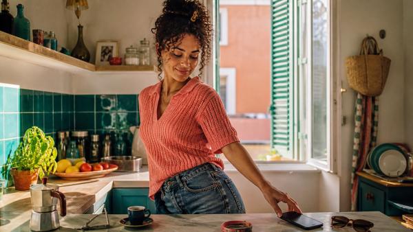 Giovane donna adulta in una cucina colorata mentre beve un espresso accanto a un telefono appoggiato sul tavolo
