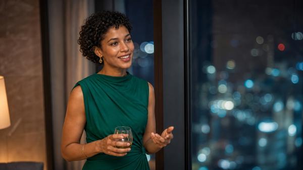 Adult woman in a green evening dress speaking naturally beside a city-lit window