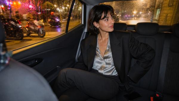 Giovane donna adulta seduta sul sedile posteriore di un taxi notturno con il telefono rivolto verso il basso
