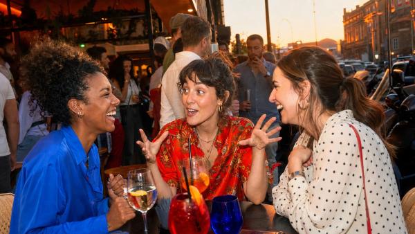 Tre giovani donne adulte che ridono insieme durante un aperitivo serale